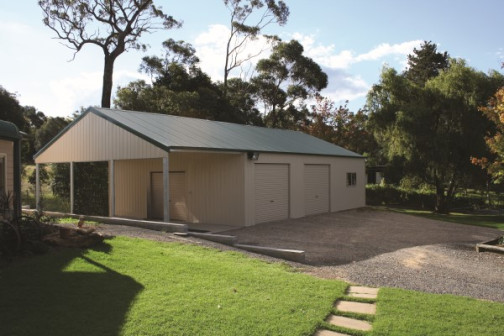 A large garage in cream with a green gable roof, a large garaport on one end and two single roller doors on the side