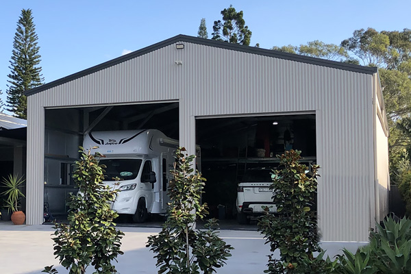 A large residential garage with two roller doors, including a larger one to the left where a caravan is parked inside