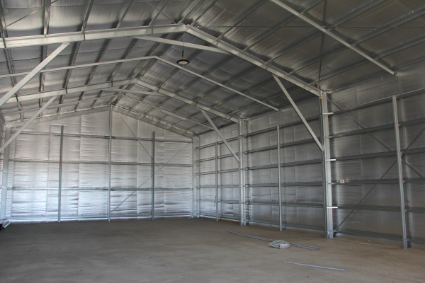 Interior view of a steel gable roof shed with a concrete floor showing the framework and insulation
