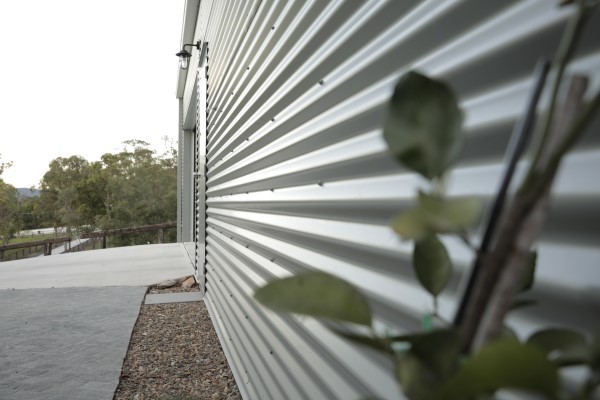Close up of the corrugated steel on the side wall of a farm shed with a concrete driveway and some out of focus plants in the foreground