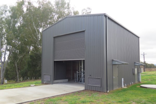 A grey shed with a large single roller door with the industrial equipment inside just visible through the half open door.