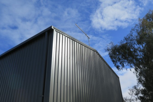 An upwards angled shot of a grey gable shed wall against a blue sky