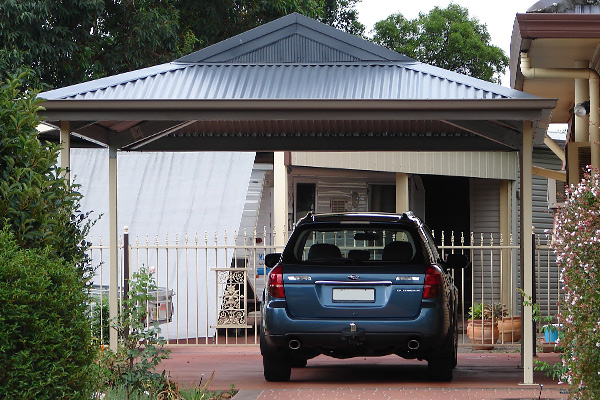 Car parked beneath dutch gable carport in dark grey with cream supports