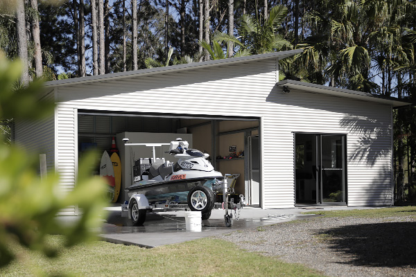 Skillion or monopitch roof garage with open double roller door, sliding glass door on the lean-to and a jetski on trailer being washed in the driveway