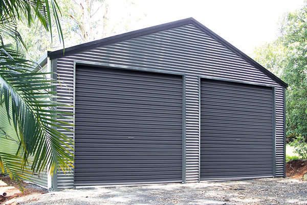 Grey shed with gable roof and two roller doors with palm fronds in foreground