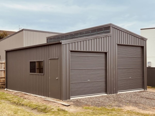 A brown skillion roof garage with a lean to and two roller  doors